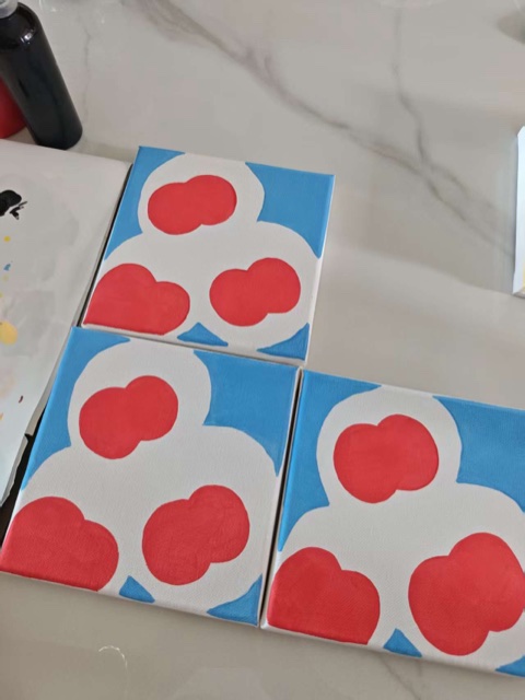 Red apple shapes being painted entirely by hand in acrylic on blue-and-white canvases